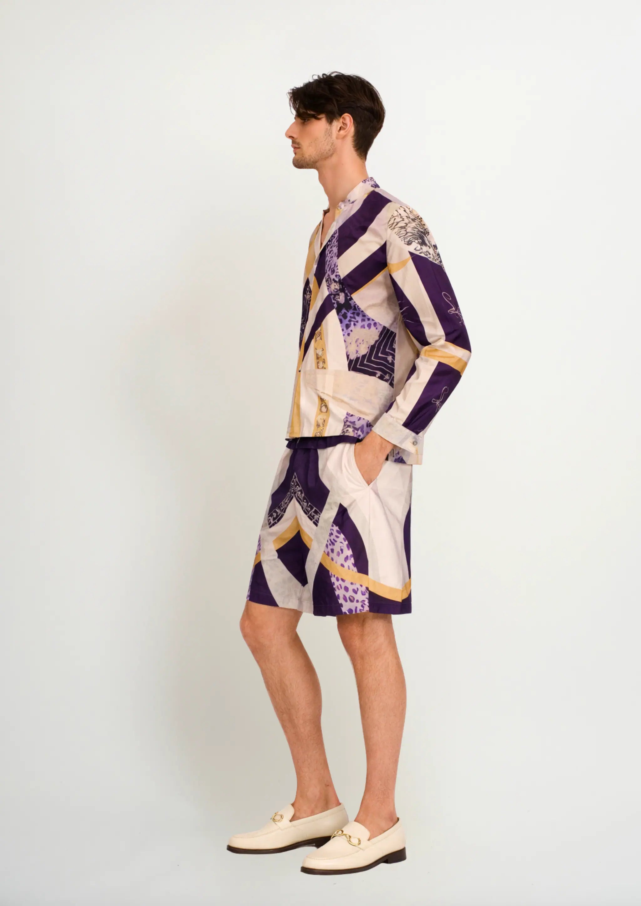 Side profile view of a model showcasing a men's luxury silk blend Korean collar shirt and matching resort shorts by Korè Collections in the Blooming Night pattern, paired with cream leather loafers.