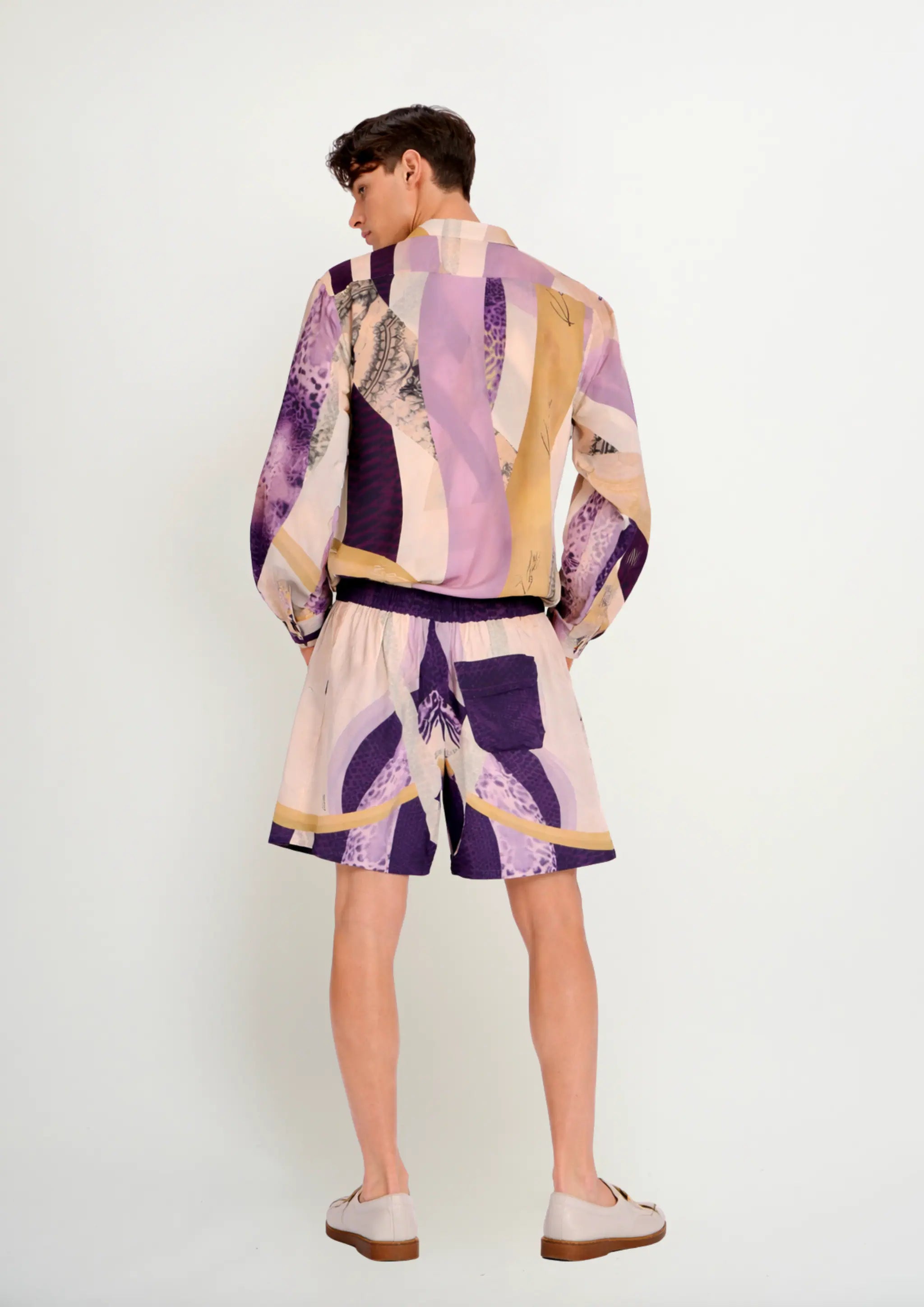 Back view of a model in a luxury men's silk blend long-sleeve shirt with a Korean collar and matching resort shorts by Korè Collections, highlighting the Blooming Night pattern alignment and a single back pocket on the shorts.